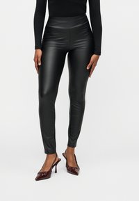 Μαύροι κολάν από τεχνητό δέρμα με ψηλή μέση, λεία υφή, εφαρμοστή γραμμή και μήκος μέχρι τον αστράγαλο, σε συνδυασμό με μπορντό μυτερά τακούνια.