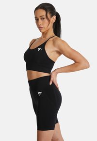 Zwarte atletische crop top en high-waisted shorts gemaakt van rekbare stof. Kenmerkt zich door een logo, een strakke pasvorm en een gladde textuur.