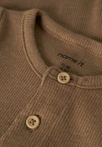 Brown ribbed fabric top with a round neckline, featuring two buttons and a care label with brand name “name it” in the center.