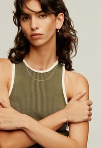 Collares de plata superpuestos sobre una camiseta verde con textura acanalada, con un colgante circular. Una pulsera de plata con acentos de estrellas en la muñeca.