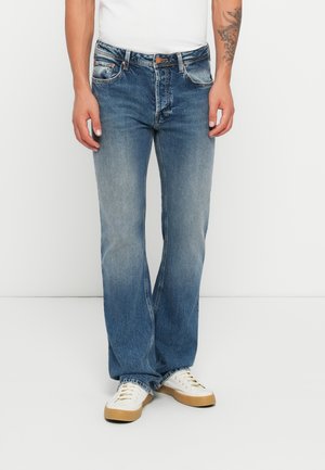 Jeans de mezclilla azul con un corte relajado, ligera decoloración, diseño de cinco bolsillos y cierre de un botón. Combinados con zapatillas blancas.
