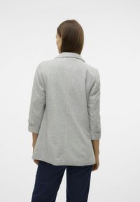 Blazer gris au design ajusté, avec un col cranté et des manches trois-quarts. Le tissu semble lisse avec une texture légère.