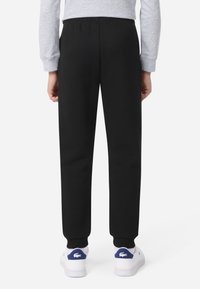 Schwarze Jogginghose mit elastischem Bund, zulaufenden Bündchen und glatter Textur, kombiniert mit weißen Turnschuhen mit blauen Akzenten.