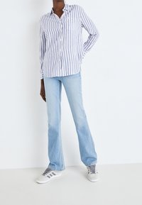 Blauw-wit gestreepte overhemd met lange mouwen en een button-down kraag, gecombineerd met lichtblauwe flared jeans en grijs-witte sneakers.