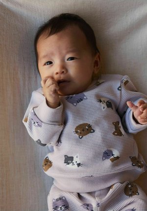 Lyse lilla sweatshirt med vaffeltekstur og dyremønster, der viser katte og hunde. Babyen sutter på en finger, foran en neutral baggrund.