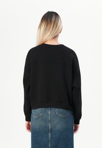 Sweatshirt noir coupé avec un col rond et des manches longues, associé à une jupe en denim bleue avec des poches arrière et une coupe droite.