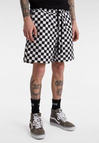 Black and white checkered swim shorts with an elastic waistband and drawstring. Worn with grey high-top sneakers and black socks.