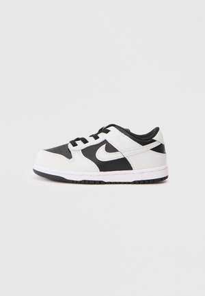 Basket Nike basse noire et blanche avec lacets, logo swoosh sur le côté, et semelle en caoutchouc sur un fond clair uni.