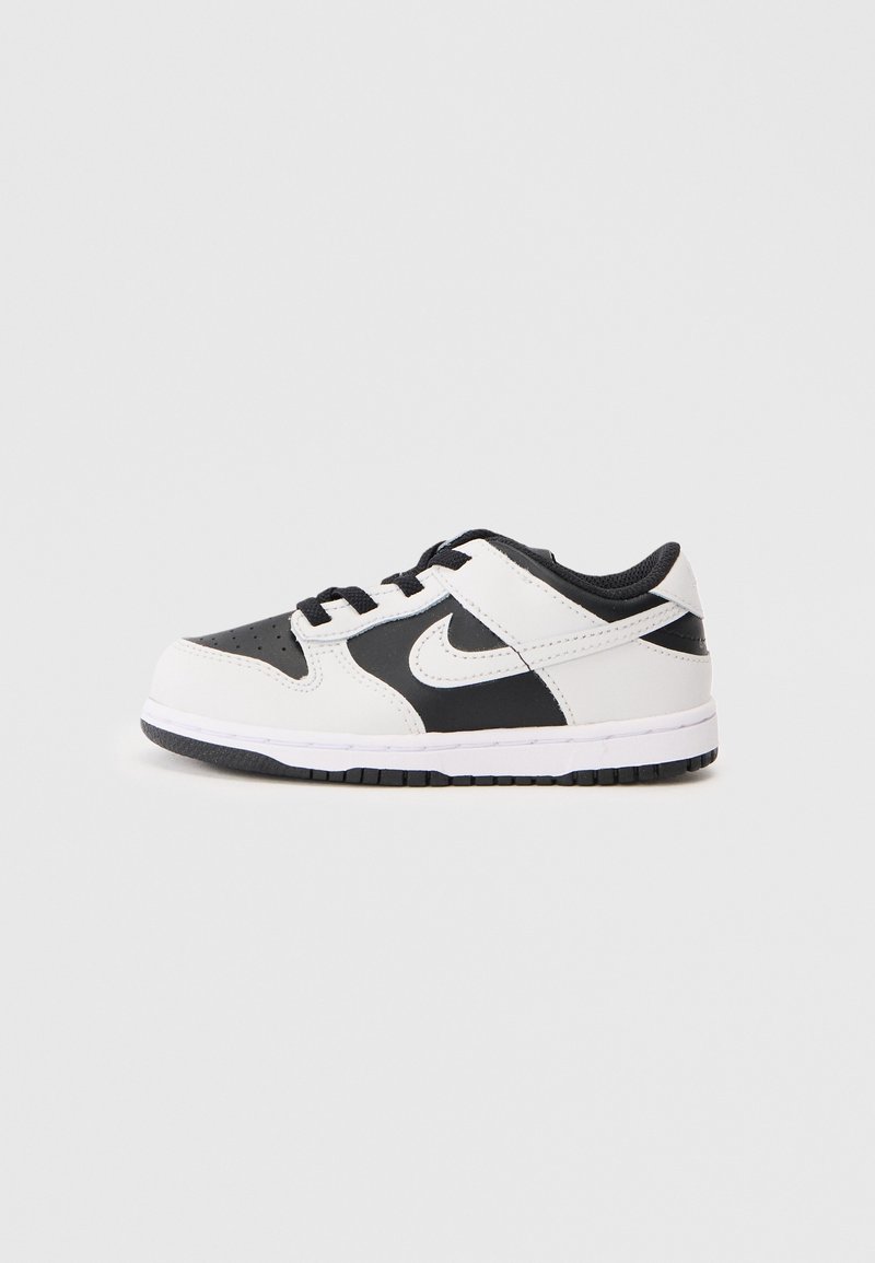 Basket Nike basse noire et blanche avec lacets, logo swoosh sur le côté, et semelle en caoutchouc sur un fond clair uni.