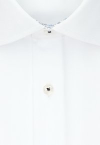 Camicia bianca con colletto a punte, caratterizzata da una chiusura con bottone in argento lucido e un bordo decorato sul colletto interno. Tessuto dalla consistenza liscia.
