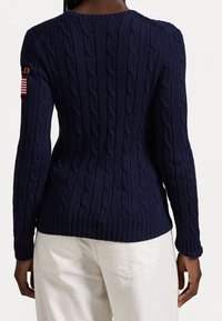 Maglione navy a coste con lavorazione a trecce, maniche lunghe, con una piccola toppa della bandiera americana sulla spalla sinistra e design aderente.