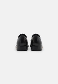 Black leather shoes featuring a smooth finish, round toe, and low-profile black rubber sole, viewed from the back.