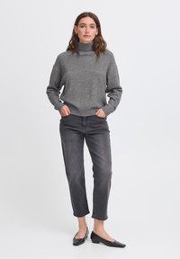 Maglione grigio a collo alto lavorato a maglia con una texture a coste, abbinato a jeans grigi e ballerine nere. Il maglione è accorciato e ha maniche lunghe.