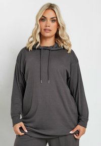 Grå ribbad hoodie med avslappnad passform, featuring dragsko i huvan och långa ärmar. Tyget har en mjuk struktur och en subtil lyster.