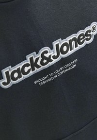 Mustus dressipluus, millel on silmapaistev valge logo "Jack & Jones", hallid aktsendid ja väike tekst all, mis ütleb "Toodud teile Org Dept. poolt."