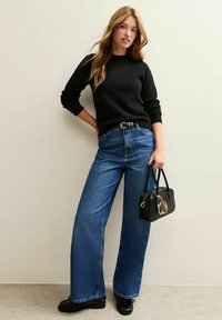 Schwarzer Pullover, hoch-taillierte blaue weite Jeans und eine kleine schwarze Handtasche mit Akzent. Das Outfit zeichnet sich durch minimalistisches Design und Texturen aus.