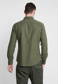 Olijfgroene blouse met knopen, lange mouwen, standaardkraag en afgeronde zoom, gemaakt van een lichtgewicht stof, met zichtbare stiksel-details op de manchetten.