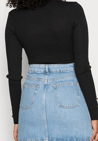 Haut noir à manches longues côtelé associé à une jupe en denim bleu clair avec poches arrière et ourlet visible.