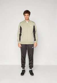 Ljusgrön zip-up jacka med svarta detaljer, matchad med svarta träningsbyxor. Båda har små vita logotyper på bröstet och låret.