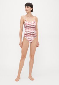 White one-piece swimsuit featuring a pattern of red hearts. Thin adjustable straps, fitted design, and smooth fabric texture.