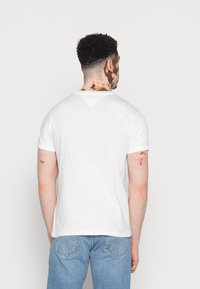 Hvid kortærmet t-shirt med en V-formet rygudskæring, lavet af blød bomuld. Båret med lyseblå denimjeans.
