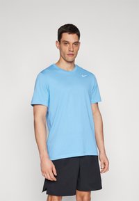 Lyseblå Nike T-skjorte med korte ermer og rund hals, med hvit logo på venstre bryst. Brukt sammen med svarte shorts. Glatt stofftekstur.