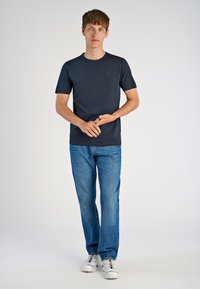 Marinblå bomullst-shirt med korta ärmar och rund halsringning, ihopparad med ljusblå denimjeans. Modellen står med händerna hopknäppta.