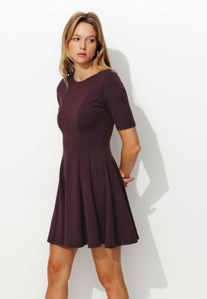 Robe violette à manches courtes avec un corsage ajusté et une jupe évasée, comportant des coutures verticales et un col rond. Texture de tissu lisse.