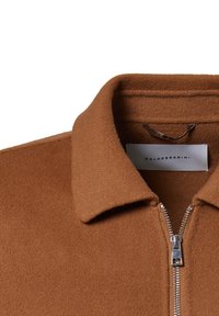 Brown fleece jacket with a pointed collar and silver zipper. The fabric appears soft and textured, featuring a tag with the brand name.