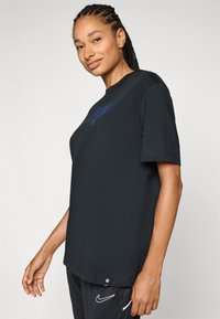Black cotton t-shirt with a relaxed fit, crew neckline, short sleeves, and a blue Nike logo on the front. Smooth texture, minimal design.