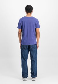 Lilla puuvillane T-särk, millel on lõdvestatud lõige, lühikesed varrukad ja ümmargune kaelus, kombineerituna lõdva sinise teksapükstega.