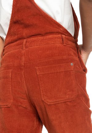 Salopette in corduroy marrone con un motivo testurizzato e a coste, dotata di tasche posteriori e spalline regolabili. Il materiale appare morbido e resistente.