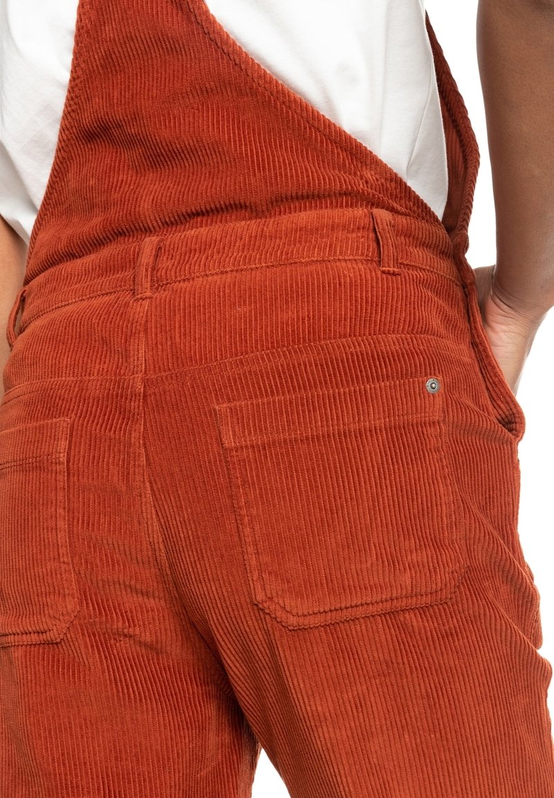 Salopette in corduroy marrone con un motivo testurizzato e a coste, dotata di tasche posteriori e spalline regolabili. Il materiale appare morbido e resistente.