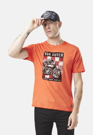 T-shirt en coton orange avec un imprimé graphique d'un pilote de moto, texte noir, manches courtes et coupe décontractée.