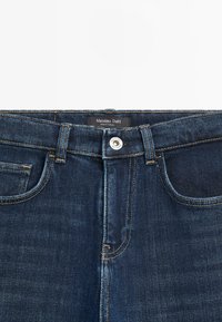 Tmavě modré džíny z denimu s klasickým designem pěti kapes, zdobené oranžovým prošíváním a stříbrným knoflíkem, s označením Massimo Dutti.