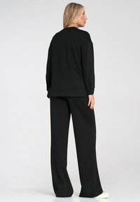 Czarna bluza z długim rękawem i szerokimi spodniami wykonanymi z miękkiego materiału, o luźnym kroju i minimalistycznym wzornictwie.