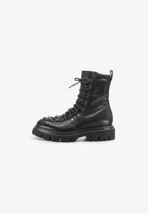 Stivale alla caviglia in pelle nera con suola spessa, dotato di lacci intrecciati, hardware in metallo e colletto in maglia testurizzata. Design durevole e robusto.