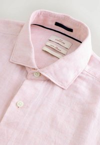 Lichtroze linnen overhemd met een button-down kraag, met een getextureerde stof en een label waarop "100% Linnen" en "SIGNATURE" staat.