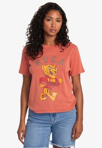 Camiseta de manga corta naranja con un dise�ño de tigre de dibujos animados y el texto "RVCA" arriba. Tela suave, corte relajado y cuello redondo.