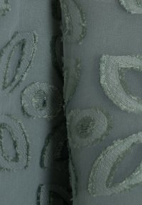 Tejido de color verde claro con patrones de bucles texturizados. El diseño incluye formas circulares y ovaladas con un efecto bordado en capas.