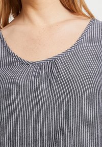 Grå och vit randig topp med rundad halsringning, prydd med en lätt rynkning i mitten och ett mjukt, texturerat tyg.