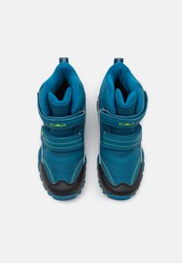 Botas de tobillo de tela azul con suelas de goma negra, que presentan dos correas de velcro y acentos de costura amarilla. Textura suave y diseño redondeado.
