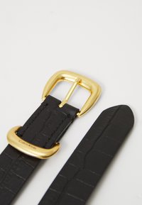 Cintura in pelle nera con un motivo testurizzato a effetto coccodrillo. Dotata di una fibbia in metallo dorato e di un passamano dorato abbinato.
