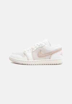 Niski biały i beżowy sneaker Nike z zamszowymi akcentami, logo Nike, sznurowaniem i gumową podeszwą, pokazany od zewnętrznej strony.