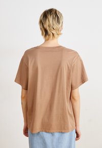 Bruine katoenen t-shirt met korte mouwen, ontspannen pasvorm, ronde hals en minimale stikseldetails, gecombineerd met een lichtblauwe denim rok.