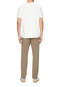 Biała bawełniana koszulka z okrągłym dekoltem, w połączeniu z beżowymi spodniami. Całość dopełniają białe trampki z jasnobrązowymi podeszwami.