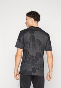 Camiseta atlética preta de mangas curtas, com um padrão hexagonal texturizado, gola redonda e tecido leve. Combinada com calças atléticas pretas.