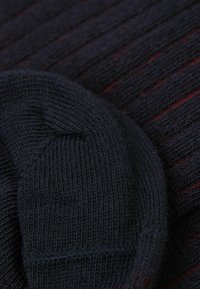 Ciemnoniebieska dziana tkanina o prążkowanej fakturze, z subtelnymi czerwonymi paskami. Zbliżenie ukazuje zaokrągloną krawędź i miękkie wykończenie.