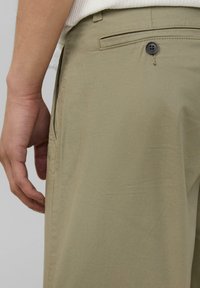 Khaki-Chinos mit einer glatten Textur, Seitentasche, Gesäßtasche mit einem schwarzen Knopf und einer taillierten Passform.