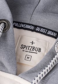 Grau Hoodie mit einem weichen Innenfutter, ausgestattet mit einem schwarzen Etikett mit weißem Text, runden silbernen Ösen und einem dekorativen weißen Kordelzug.